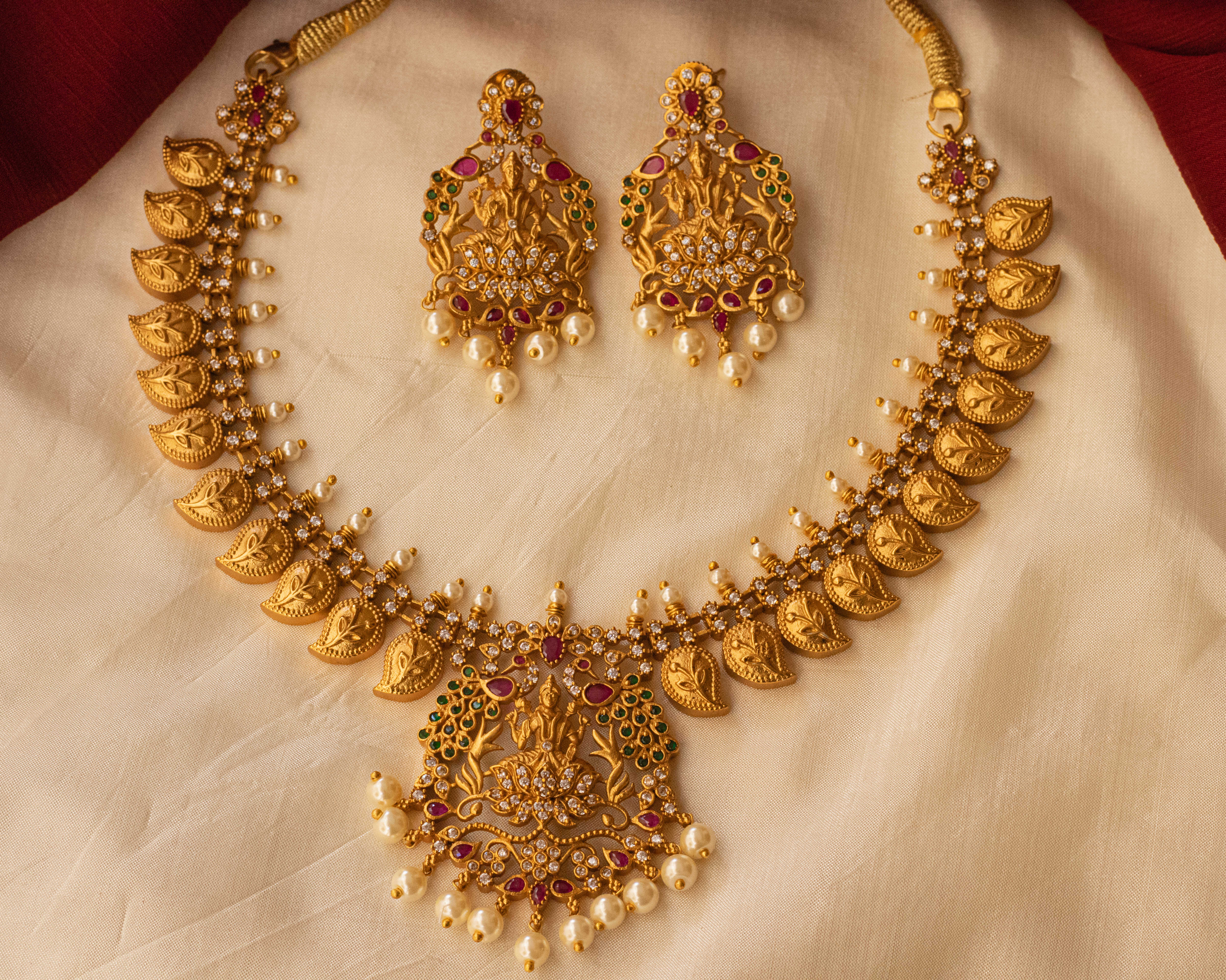  A gold necklace with matching earrings, made with diamonds, rubies, and emeralds, displayed on a cream-colored cloth.